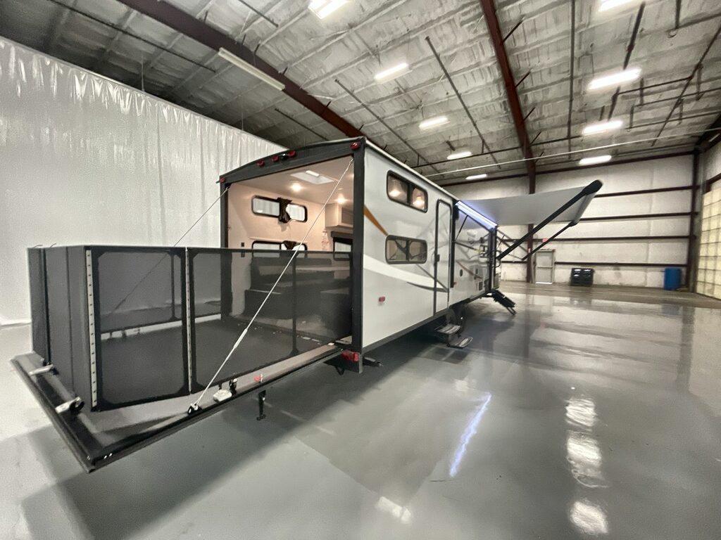 Toy hauler travel trailer shot in side a studio showing garage opened up and patio set up in the back, model wildwood fsx 280RTX