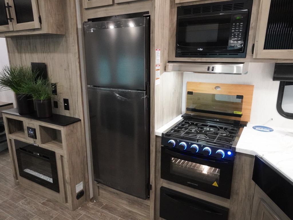 picture of the interior 287bh with oven/stove top and microwave above it, fridge, tv console with fire