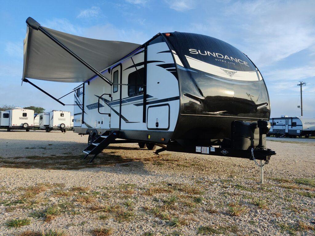 travel sundance ultra lite 294bh shot outside on gravel at golden hour, black & white fiberglass camper with awning out
